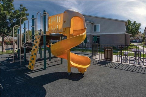 A playground with a yellow slide and a green fence.