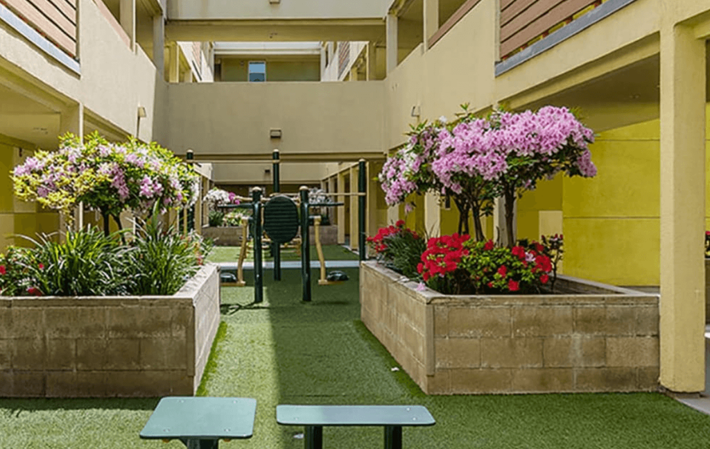A courtyard with a bench, a table and a planter with purple flowers.
