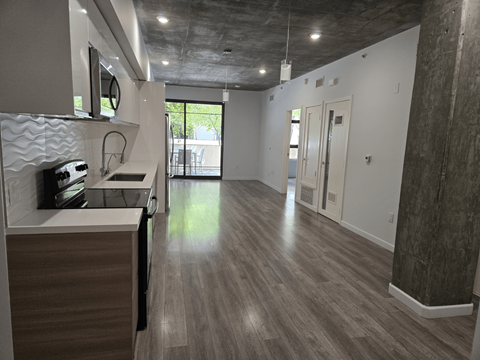 A long, narrow room with wood flooring and a kitchen area on the left side.