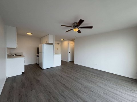 McCully Circle unit 303 spacious living room with a ceiling fan and a kitchen area with white cabinets.