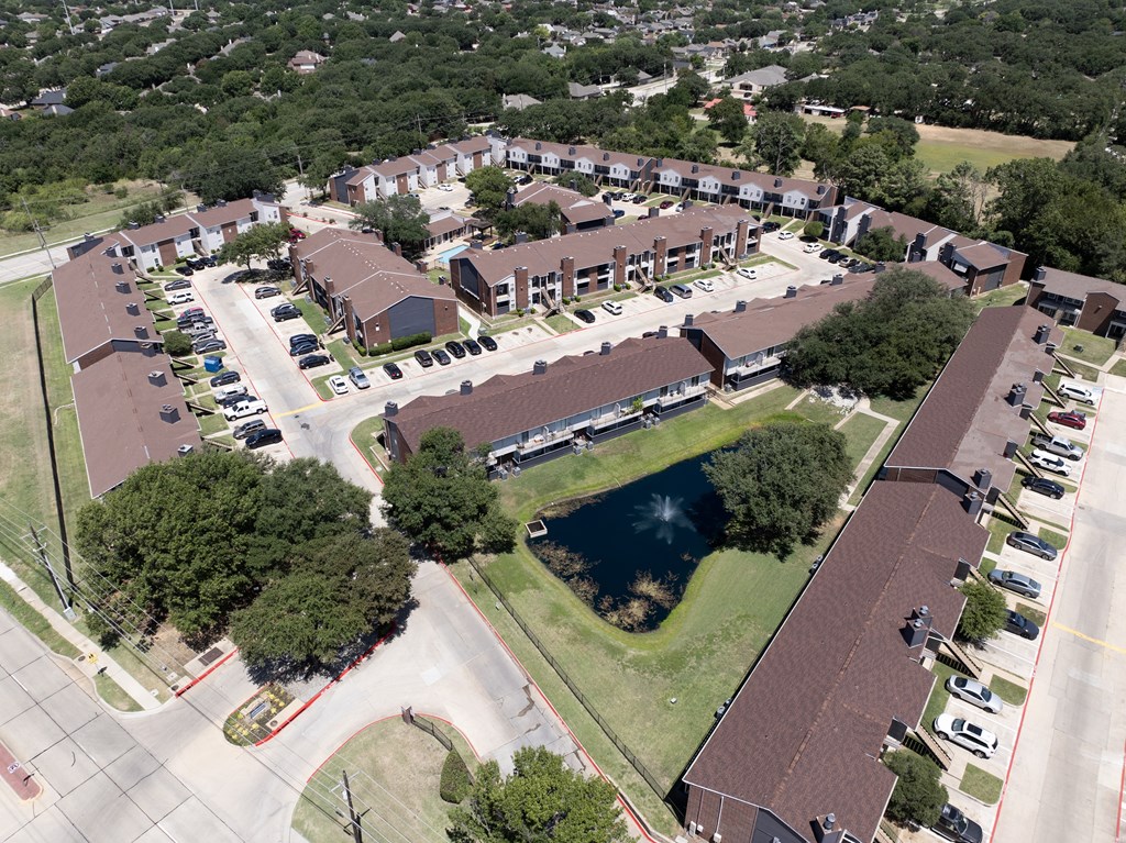 A bird's eye view of a residential complex with a pond in the middle.
