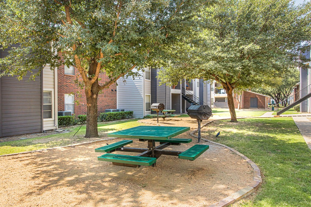 A green picnic table is in the middle of a sandy play area.