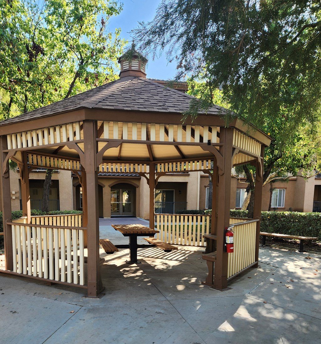 A gazebo with a table and chairs is surrounded by a wooden fence.