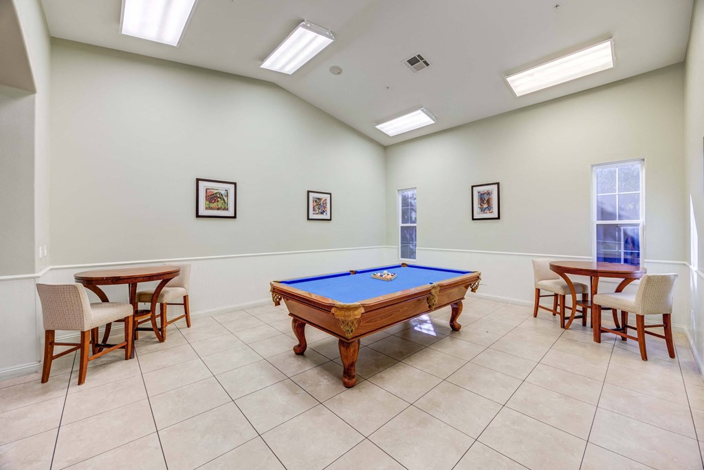 A pool table is surrounded by four chairs in a room with white walls.