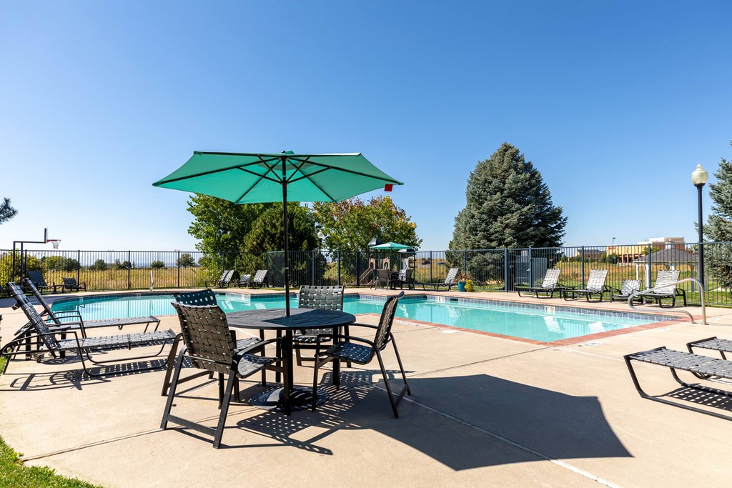 A table with chairs and an umbrella is set up by a pool.
