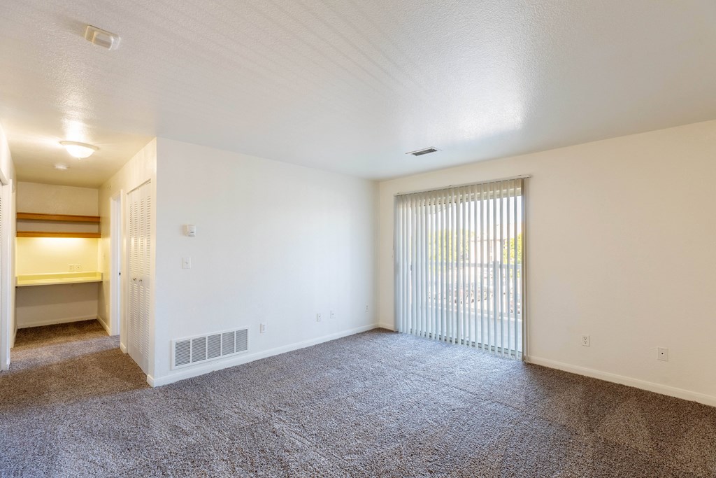 A spacious room with carpeted floor and a sliding glass door.