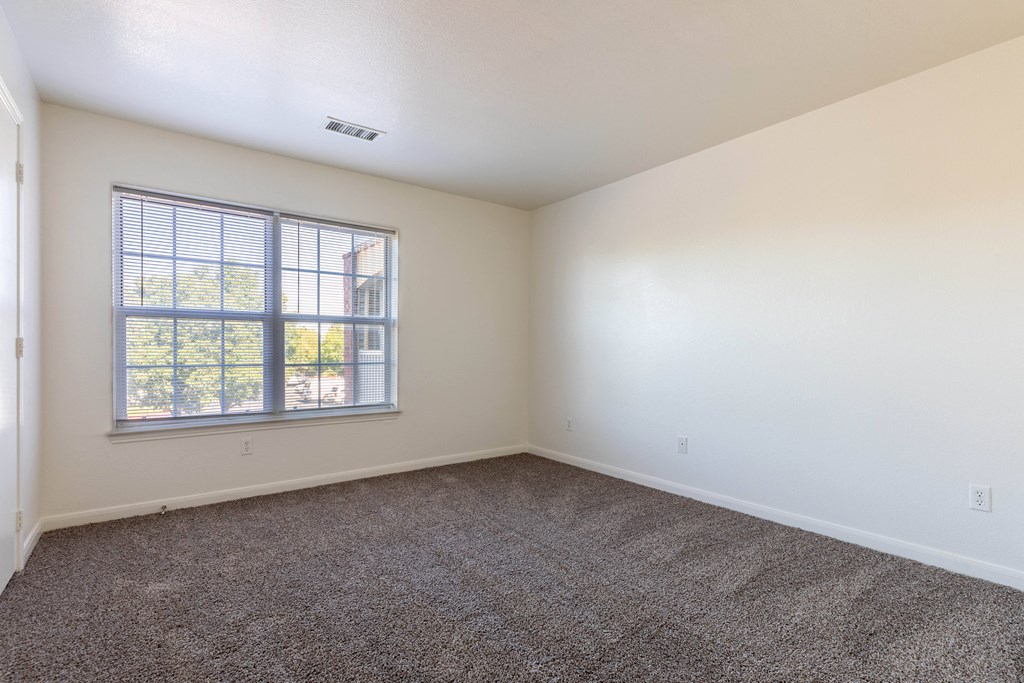 A room with a carpeted floor and a window with blinds.