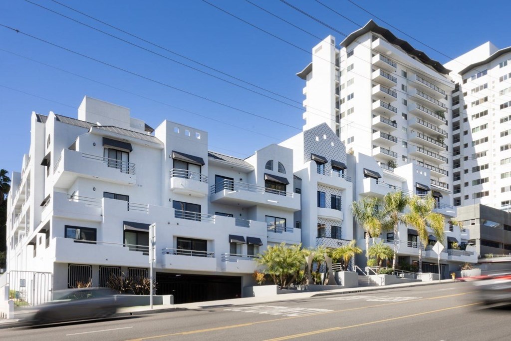 A white apartment building with a car driving by on the street.