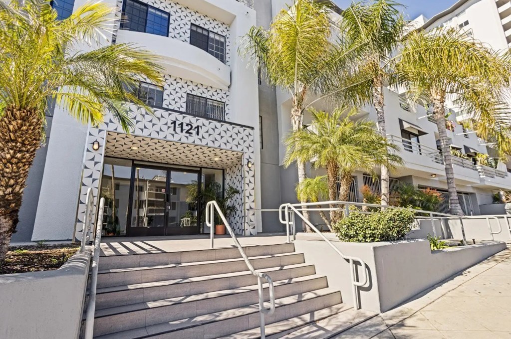 A white building with a black and white patterned entrance and palm trees in front.