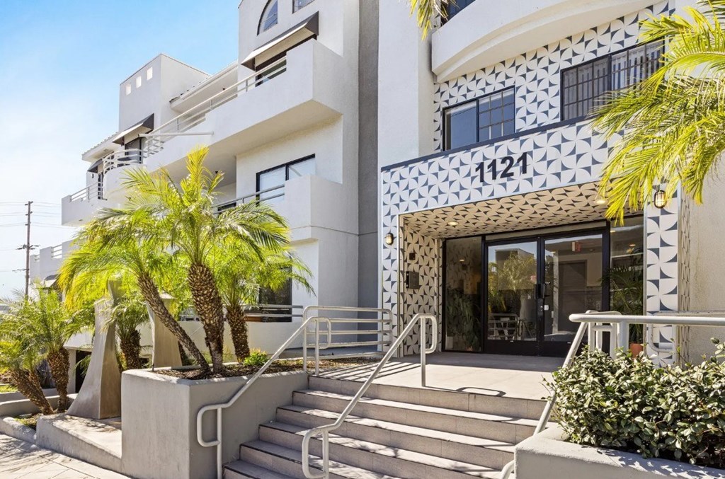 A white building with a black and white patterned wall and palm trees in front.