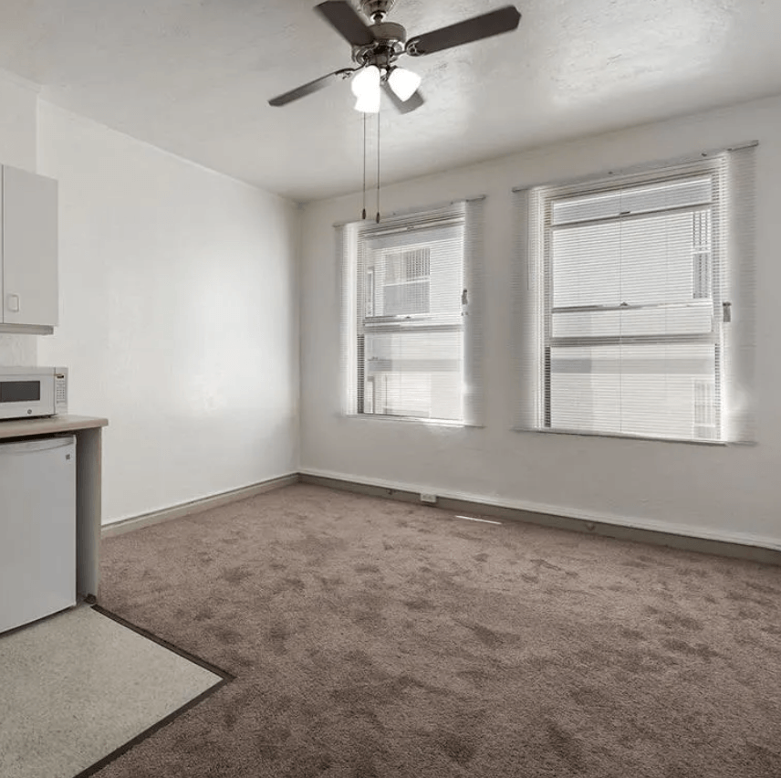 an empty room with two windows and a ceiling fan