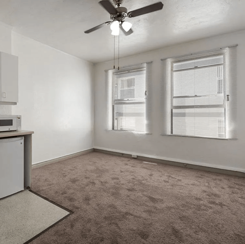 an empty living room with a ceiling fan and two windows