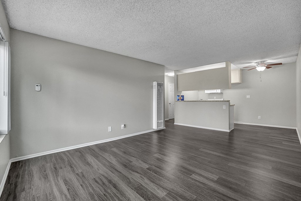an empty living room with a kitchen in the background