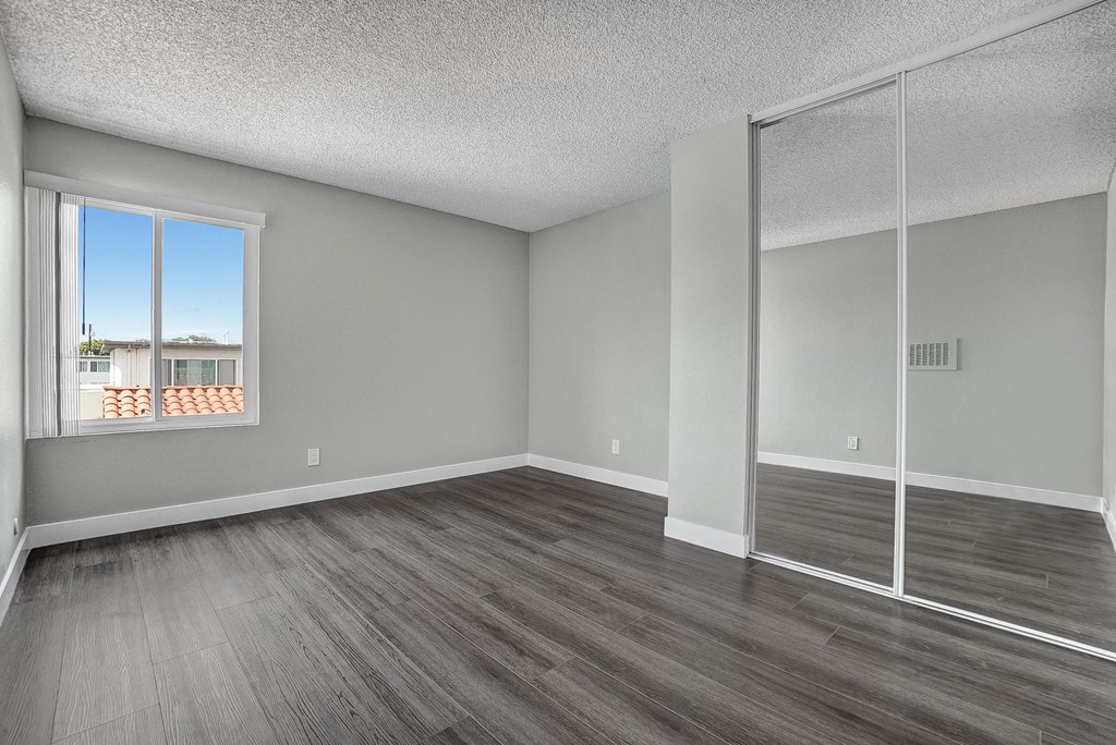 an empty bedroom with a window and mirrored closet doors