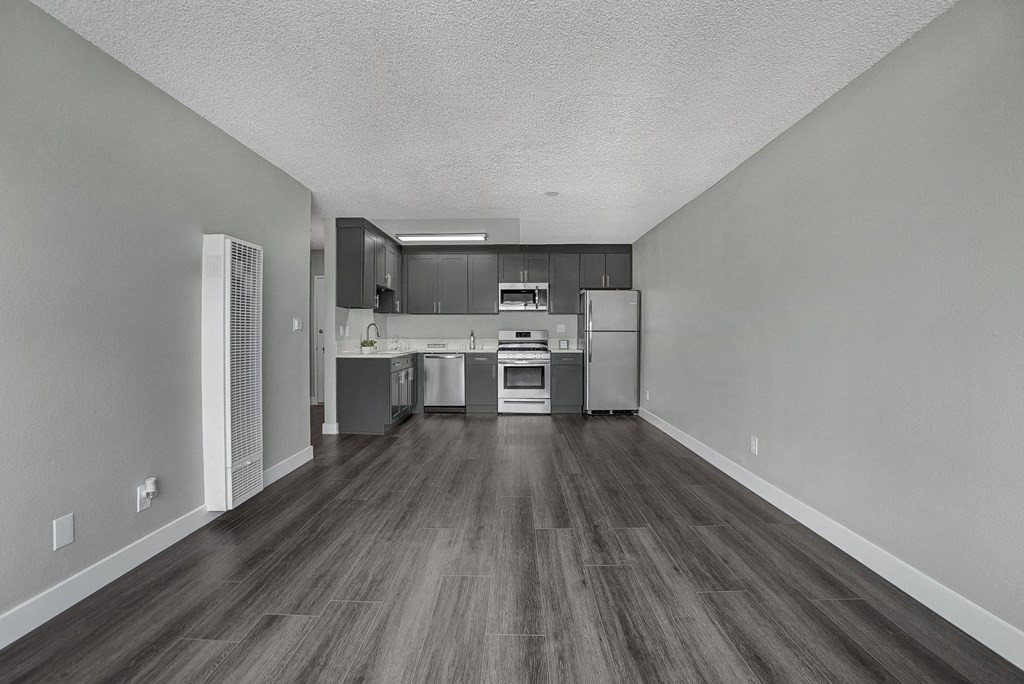 an empty kitchen and living room with hardwood floors and grey walls