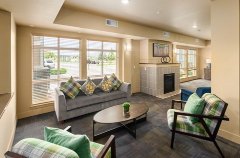 A living room with a grey couch, a green pillow, a wooden chair and a fireplace.
