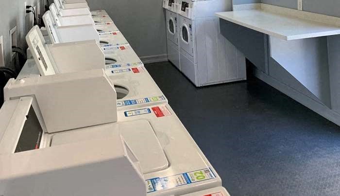 A row of white washing machines are lined up in a laundromat.