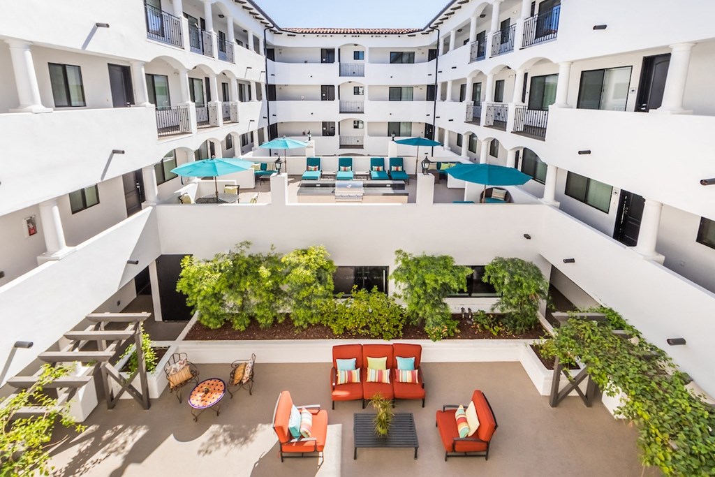 an overhead view of a hotel courtyard with orange chairs and blue umbrellas