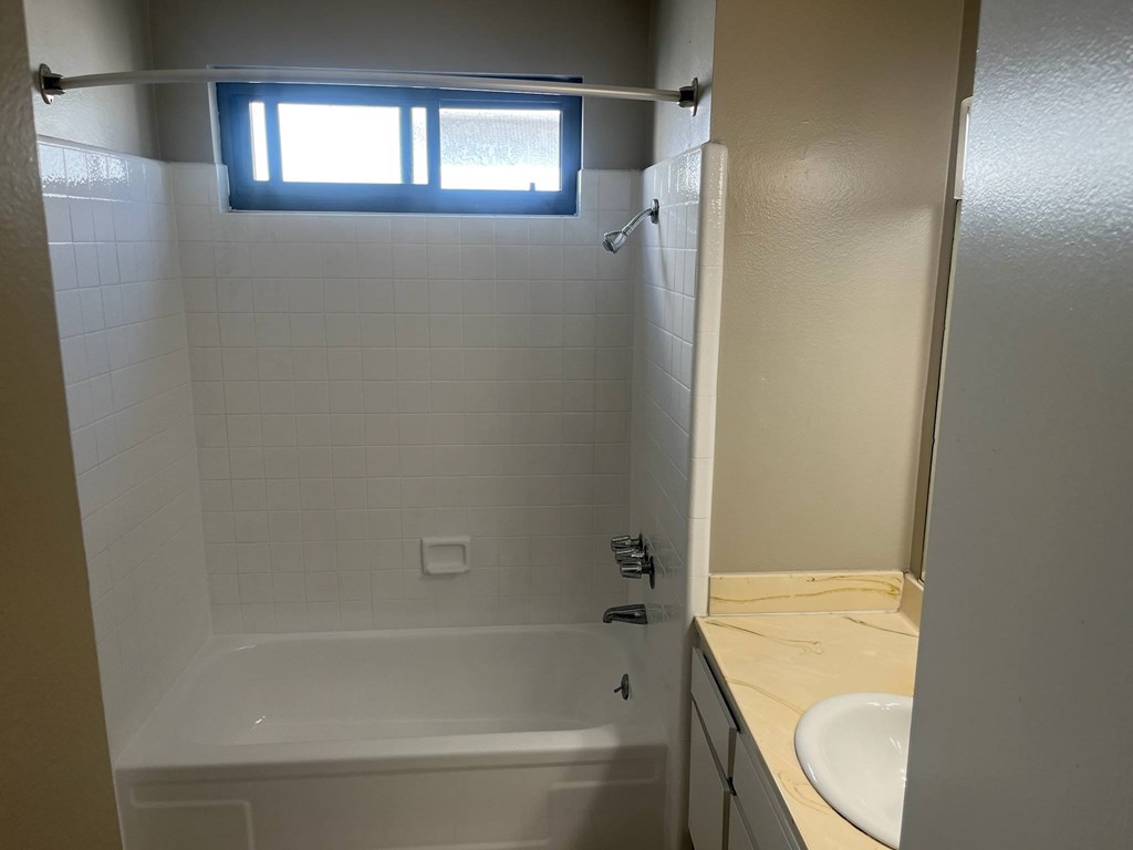 A white bathroom with a tub, sink, and window.