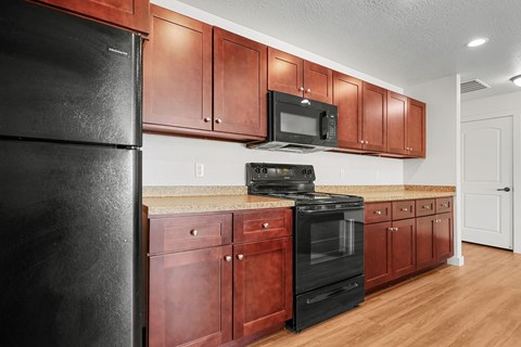 A black refrigerator is on the left in a kitchen with brown cabinets.