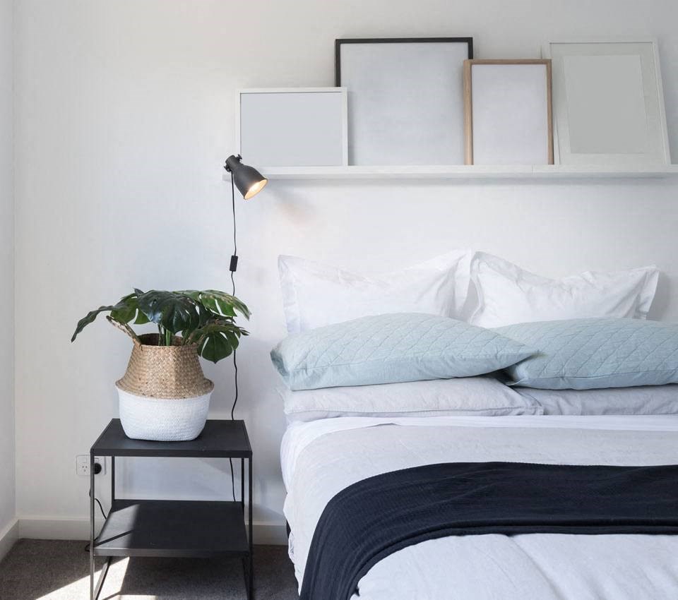 a bedroom with white walls and a bed with blue pillows and a plant