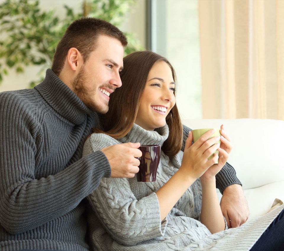 man and woman sitting on a couch holding coffee cups