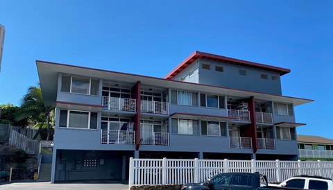 A grey building with a red roof and white fence.