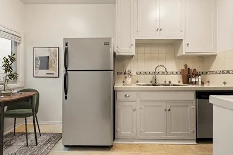 A kitchen with a refrigerator, sink, and cabinets.