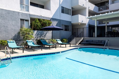 A swimming pool with lounge chairs and umbrellas in front of a building.