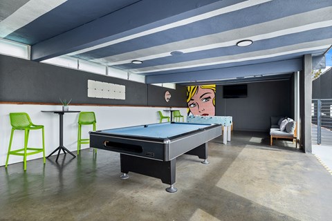 A pool table is in the middle of a room with a green chair and a plant.