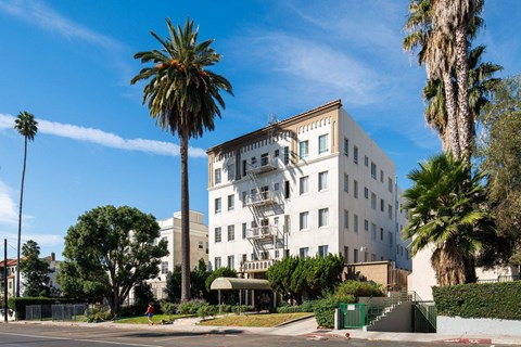 A white building with a balcony is surrounded by palm trees.