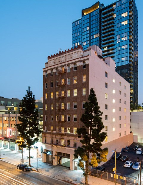 A tall building with a pinkish hue stands in front of a modern skyscraper.