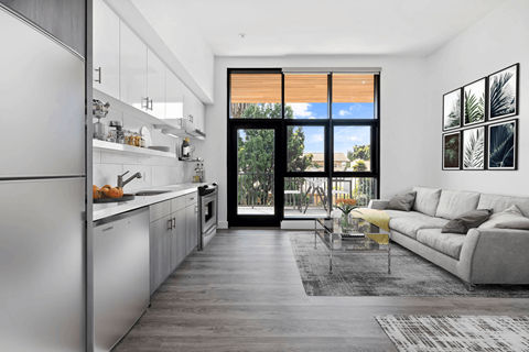 A modern kitchen with a refrigerator on the left and a living room with a couch and a coffee table on the right.