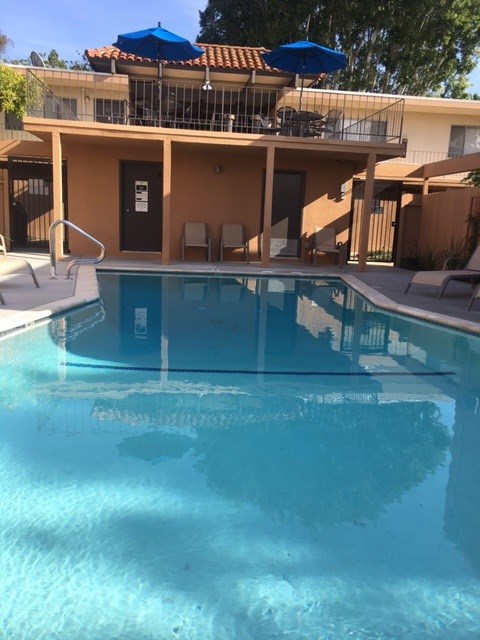A swimming pool in front of a house with a blue umbrella.