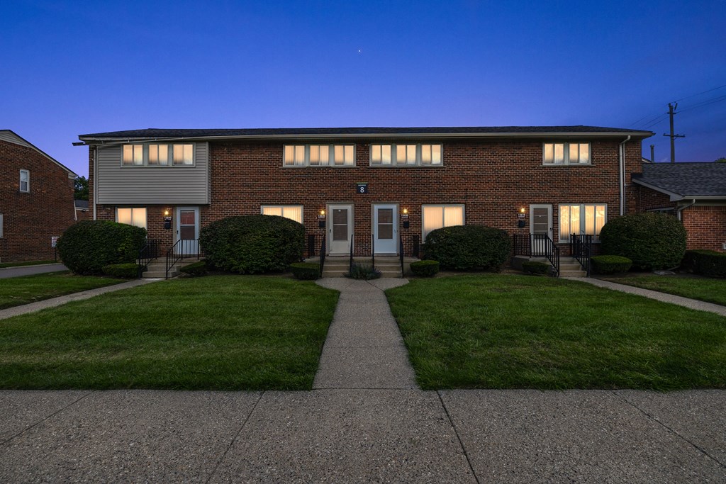 a nighttime view of a two story brick house with a walkway leading to the front door