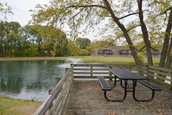 Picnic table and bench on a wooden deck by a lake.