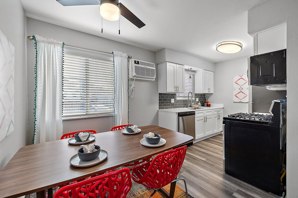 a kitchen with white cabinets and black appliances and a wooden dining table with red chairs
