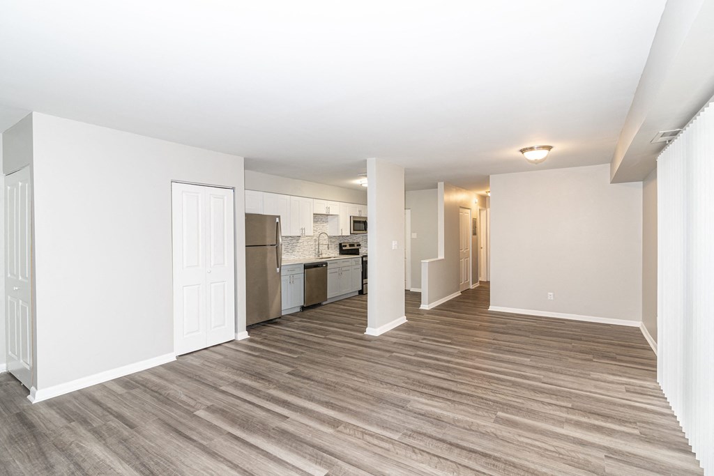 a renovated living room and kitchen with white walls and wood flooring
