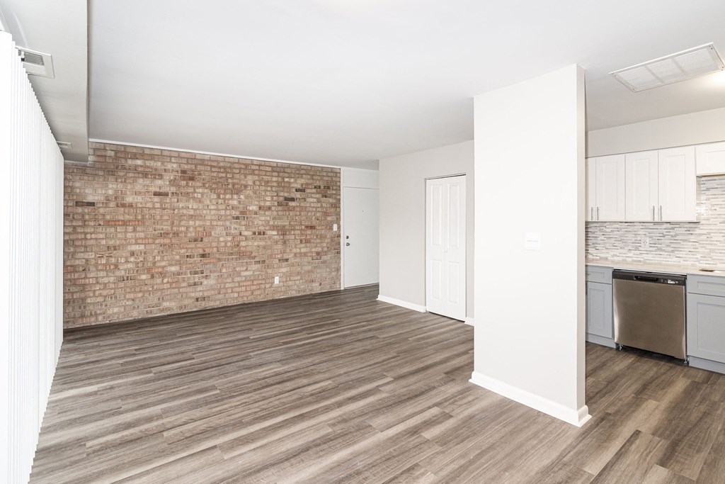 an empty living room with a brick wall and a kitchen