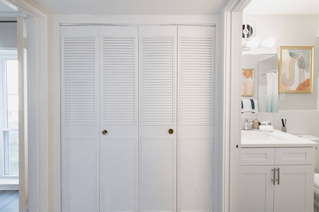 a bathroom with white cabinets and a large closet with shutters