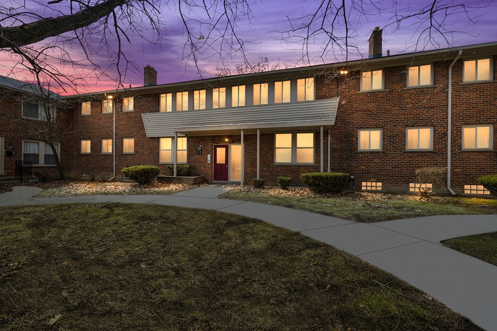a nighttime view of a brick building with a red door and a sidewalk in front of it