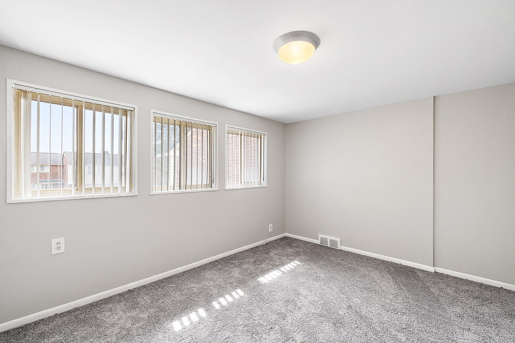 a bedroom with three windows and a carpeted floor