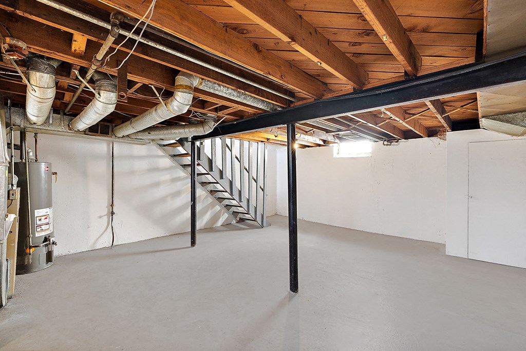 a metal stairway in a large basement with white walls and wood ceilings
