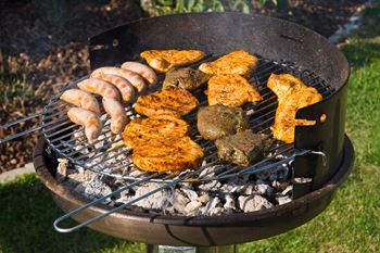 A grill with sausages, chicken, and patties cooking on it.