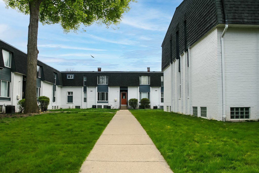 a walkway between two rows of white buildings with grass
