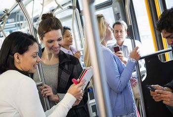 A group of people are riding in a bus, all looking at their phones.