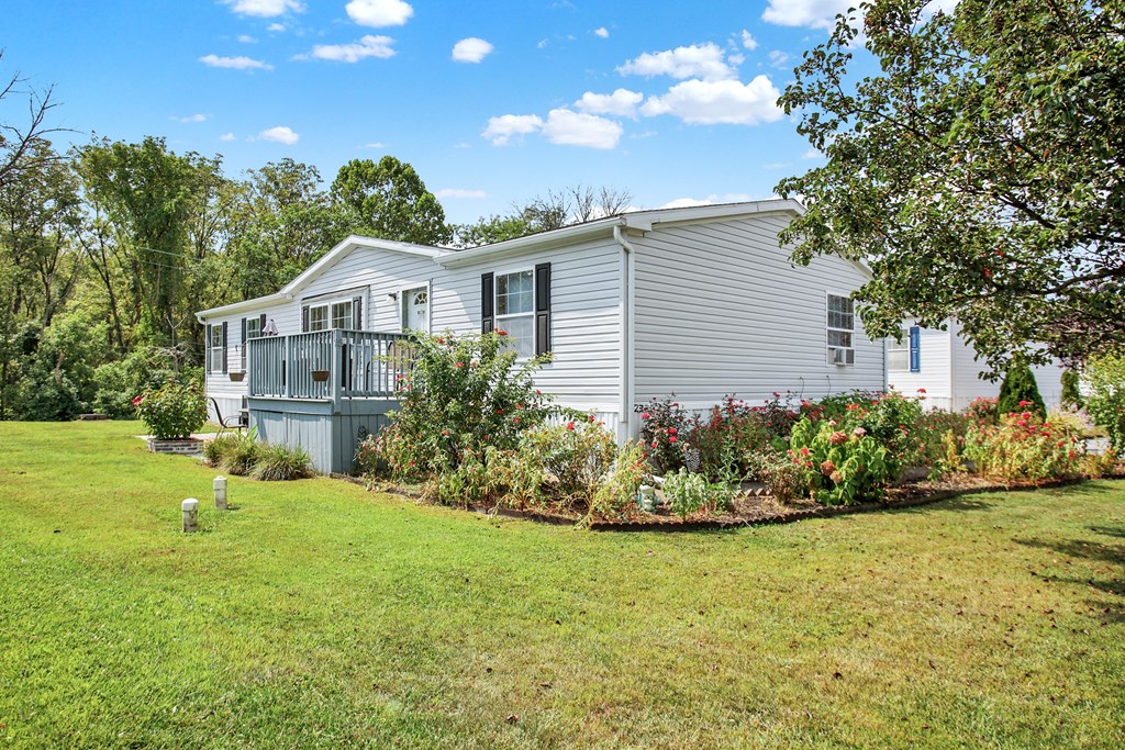 a white mobile home with a gray siding and a large garden in front of it