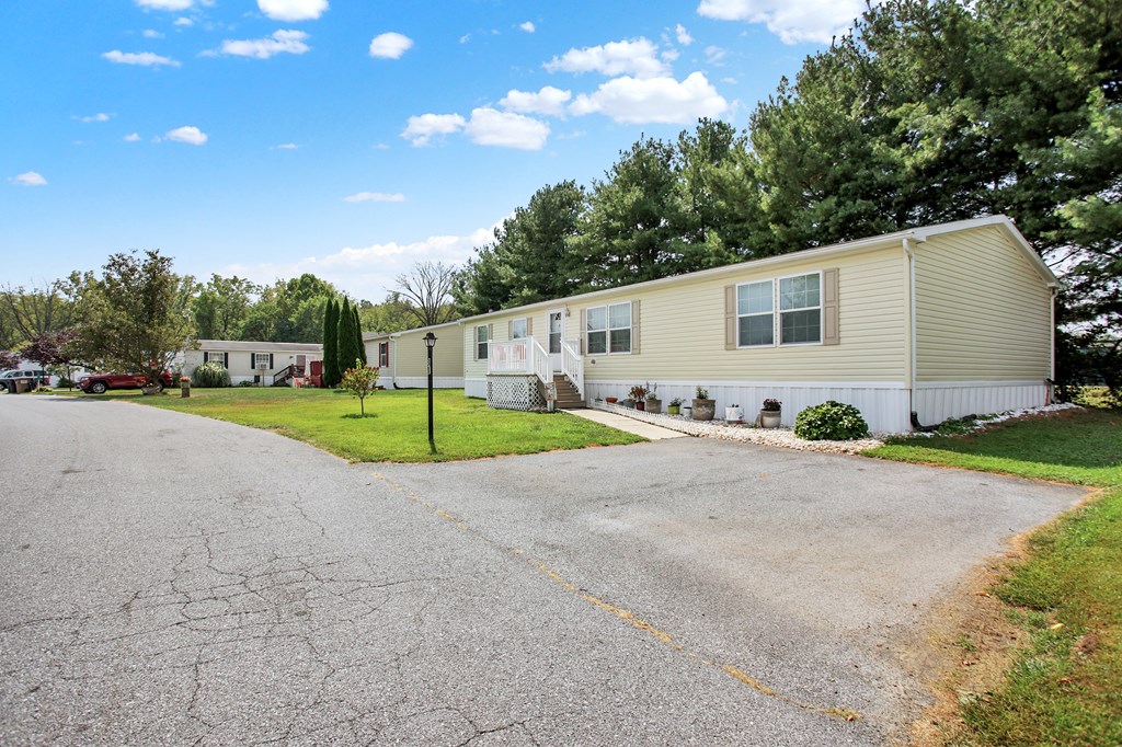 a home with a driveway in front of a yard with green grass and trees
