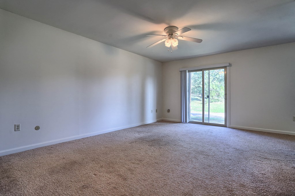 an empty living room with a ceiling fan and a sliding glass door