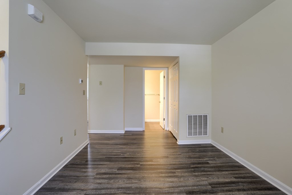 A long, empty hallway with wood flooring and white walls.
